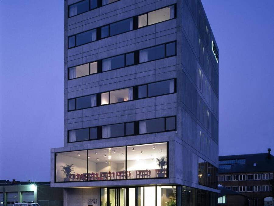 A modern hotel building with a glass facade, multiple floors, and a visible restaurant area with outdoor seating.