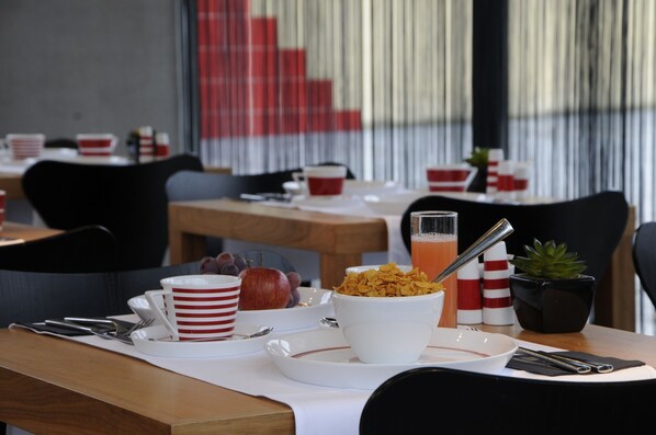 A breakfast setup with a bowl of cereal, a glass of orange juice, and a plate with an apple and grapes.