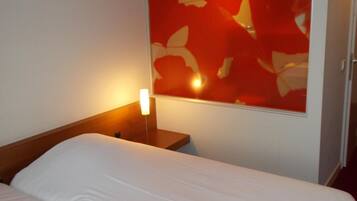 Een hotelkamer met een bed, een nachtkastje en een lamp aan de muur.