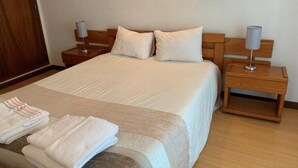Un letto rifatto con lenzuola e cuscini bianchi, una testiera in legno e due comodini con lampade.