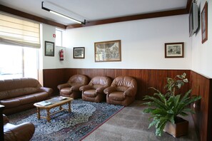 A living room with a brown leather sofa, two leather armchairs, a wooden coffee table, and a patterned rug. There are framed pictures on the wall and a potted plant. - Curia Clube Apartments (Anadia)