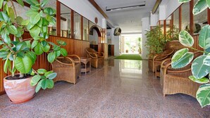 Un'ampia hall con pavimento in piastrelle lucide, mobili in vimini e grandi piante in vaso.
