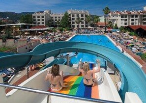 A water park with a large pool and slides, surrounded by hotel buildings and umbrellas. - Julian Club Hotel - All Inclusive (Marmaris)