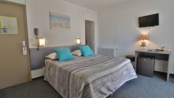 Una habitación de hotel con cama, escritorio, silla, televisión y lámpara.