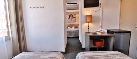 A hotel room with two beds, a desk, a television, and a refrigerator.
