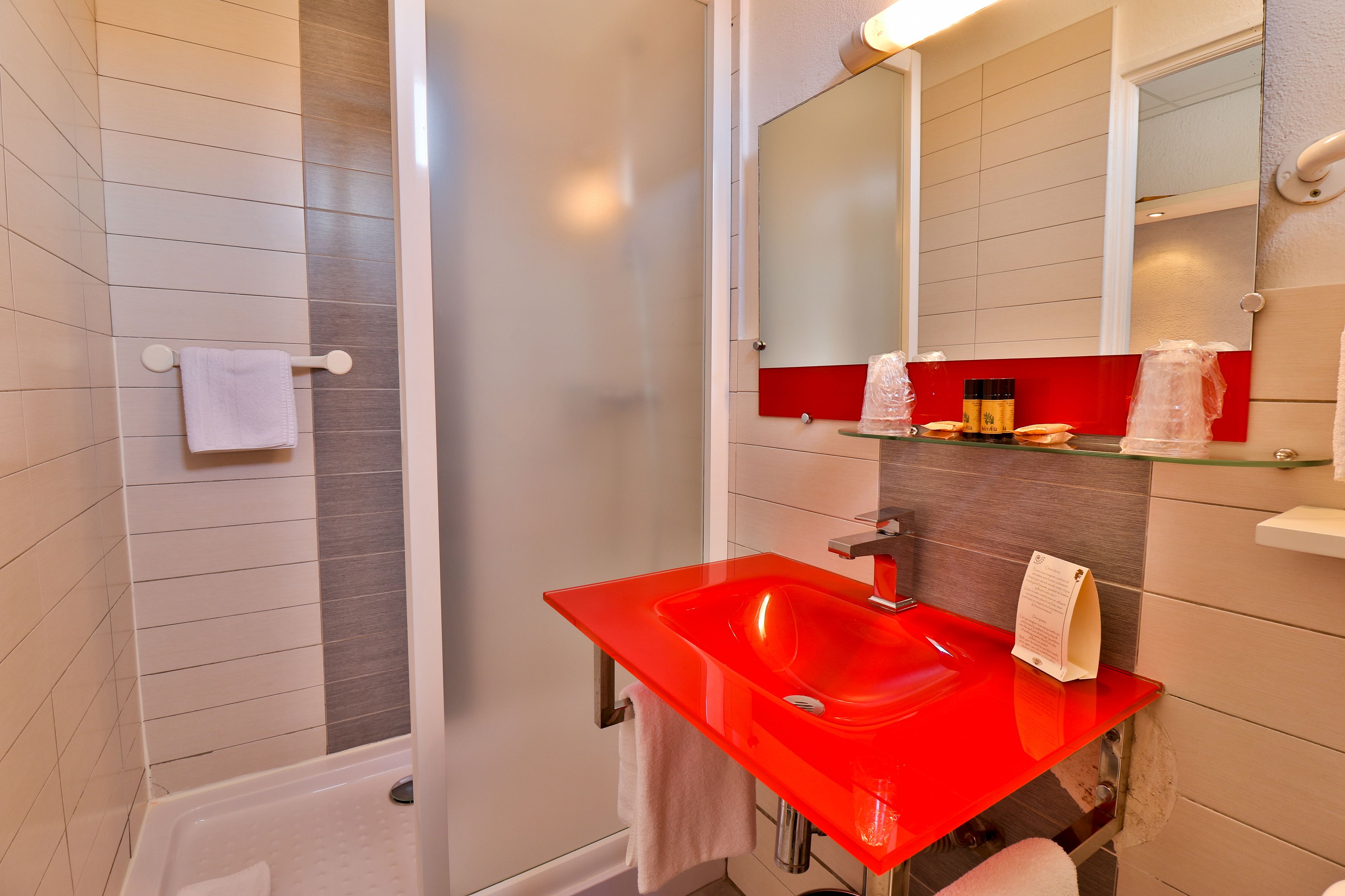 A modern bathroom with a red sink, a glass shower enclosure, and a mirror above the sink.