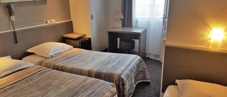 Habitación de hotel con dos camas, un escritorio, una silla, una lámpara y un teléfono en la pared.