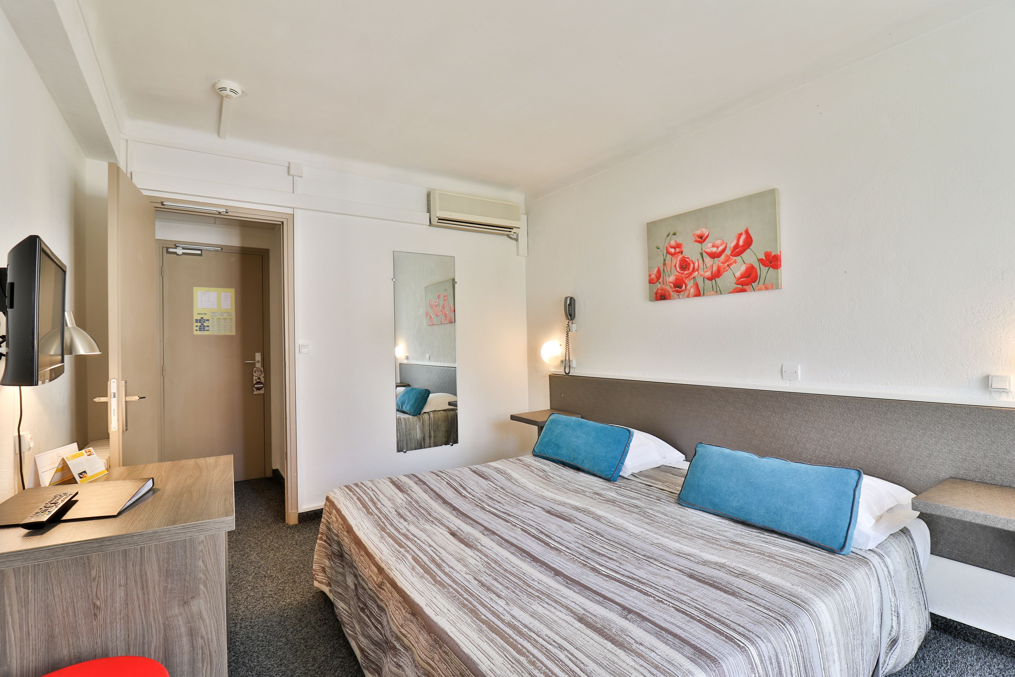 A hotel room with a bed, a desk, a chair, a TV, and a painting on the wall.