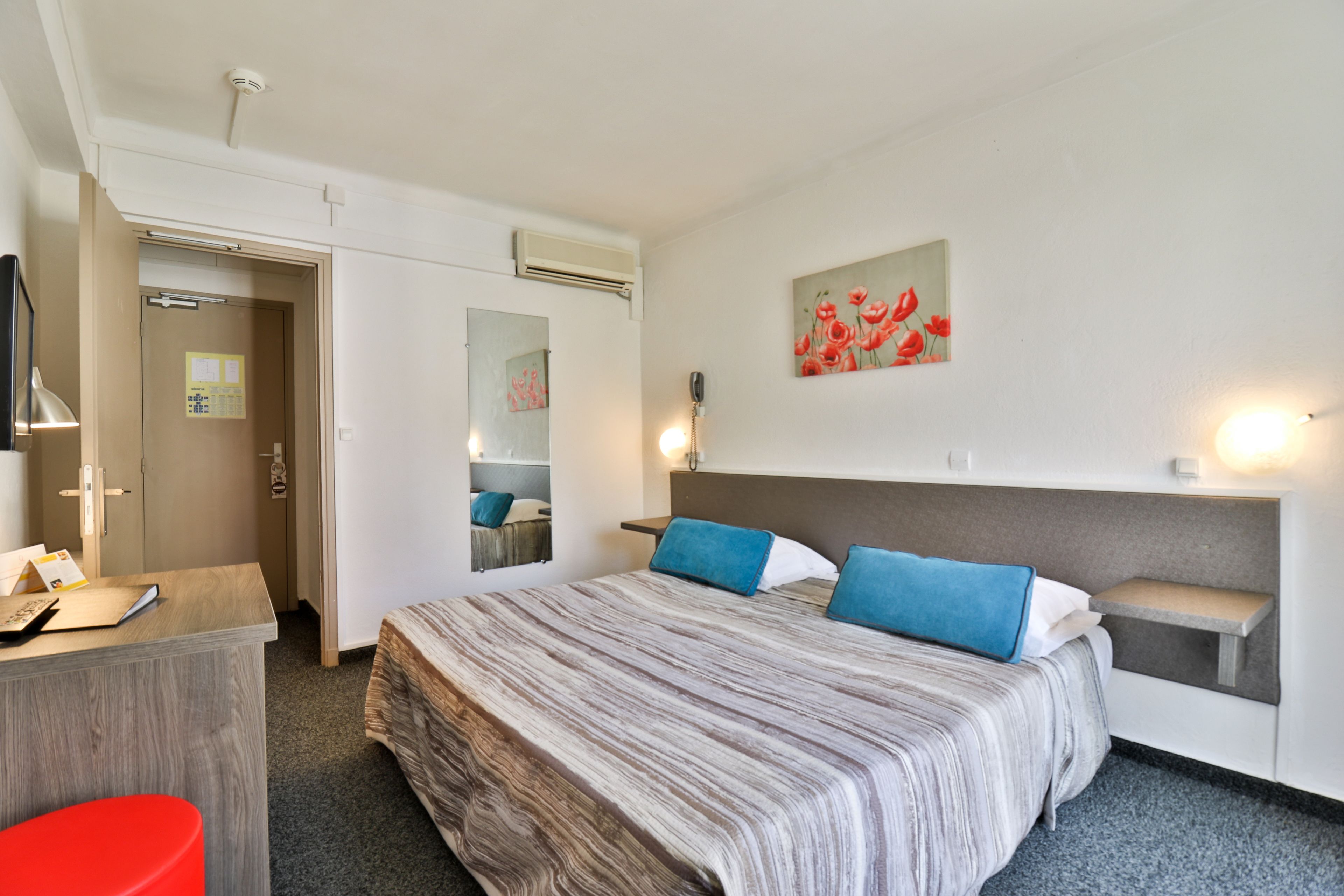 A hotel room with a bed, a desk, a chair, a mirror, and a painting on the wall.