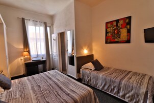 Habitación de hotel con dos camas individuales, un escritorio con lámpara, un espejo y un cuadro en la pared.