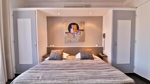 Una habitación de hotel con una cama grande, dos mesitas de noche, un teléfono en la pared y un cuadro sobre la cama.