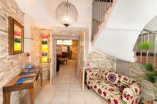 Un interior moderno con una escalera, un sofá estampado con flores, una mesa con libros y una lámpara colgante.