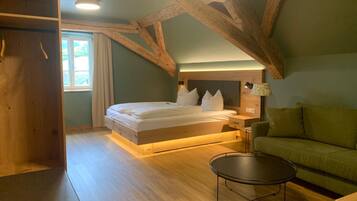 Un dormitorio con techo de madera, cama con ropa de cama blanca, mesita de noche con lámpara, sofá verde y una pequeña mesa redonda.