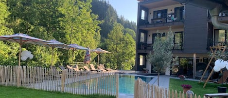 A pool area with lounge chairs, umbrellas, and a wooden fence.