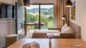 A hotel room with a balcony, a dining table with a vase of flowers, and a bed with white bedding. - Goldener Adler Oberried - Hotel & Appartements (Oberried)