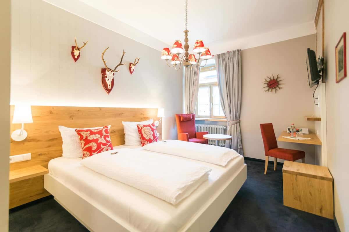 Ein Hotelzimmer mit einem großen Bett, einem Holzkopfschild, einer Kandelaber, einem Schreibtisch, einem Sessel und Wanddekorationen, darunter Tierknochen.