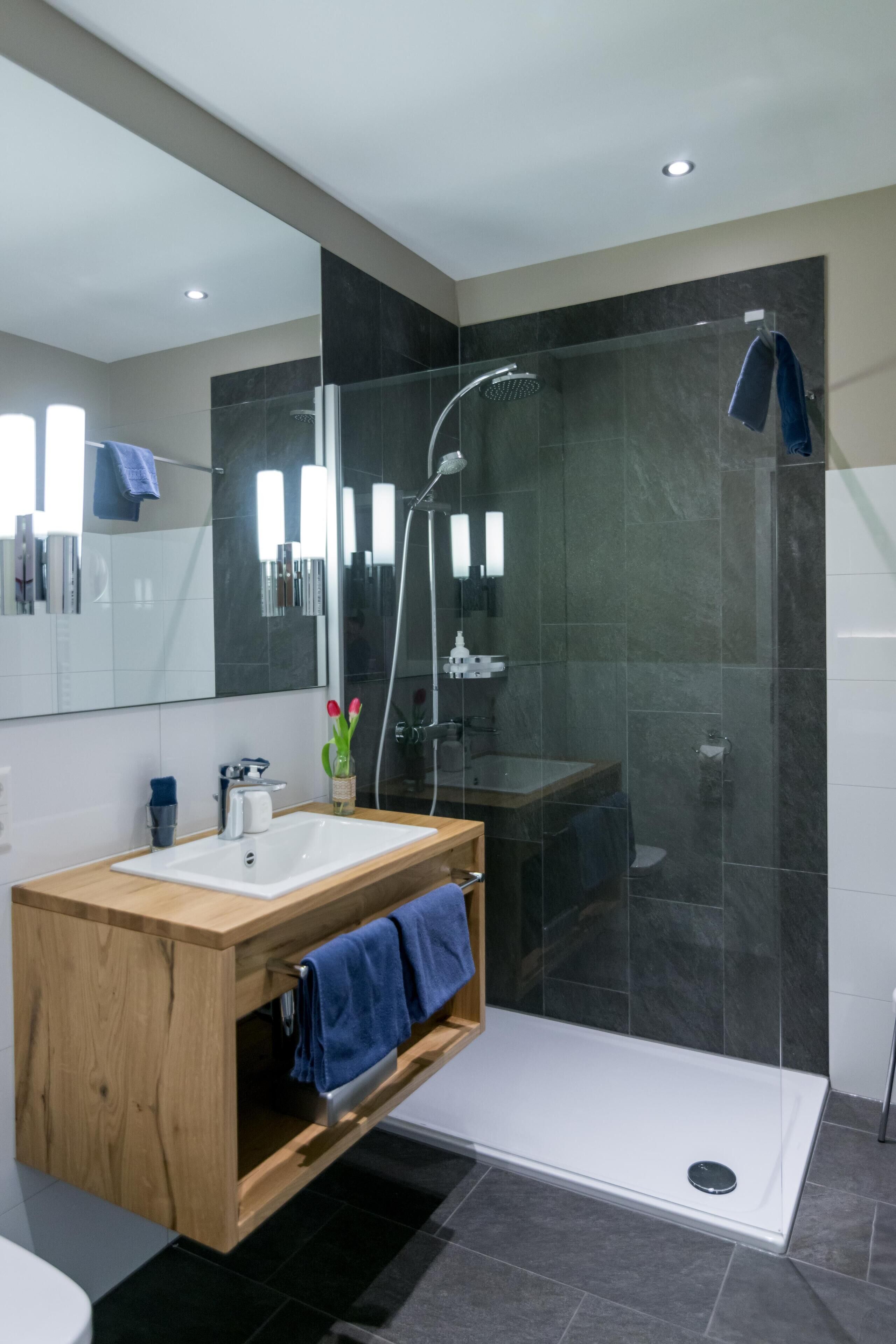 A modern bathroom with a wooden vanity, a glass shower enclosure, and a large mirror.