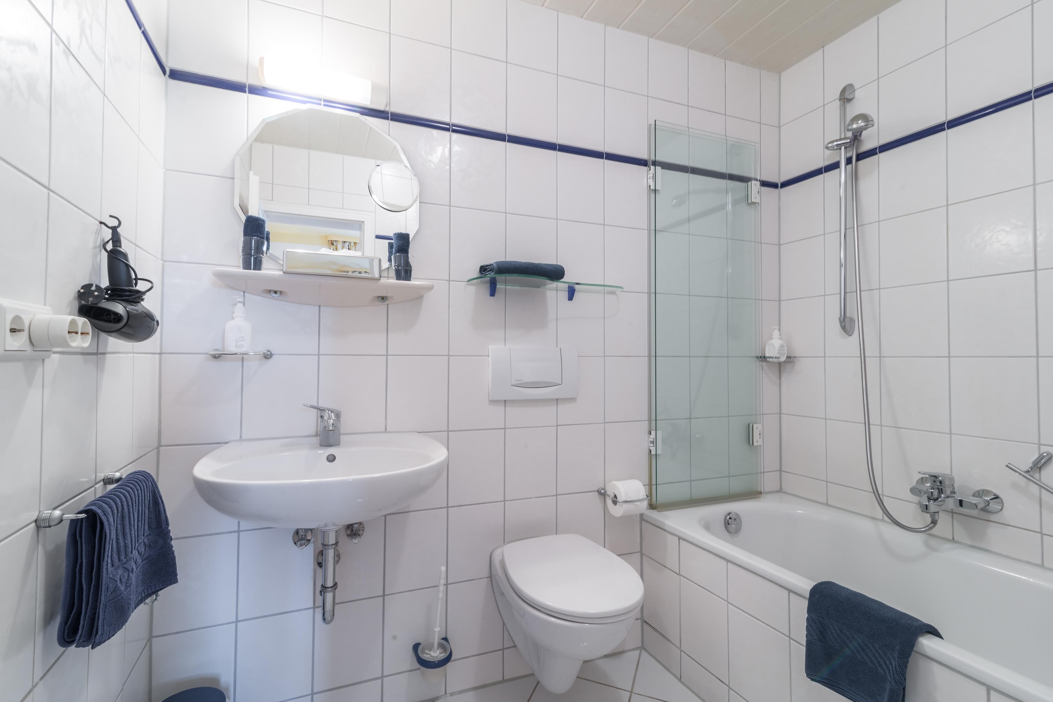 Un baño moderno con lavamanos, inodoro y bañera blancos. Cuenta con una cabina de ducha de vidrio y un espejo sobre el lavamanos.