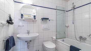 Un baño moderno con lavamanos, inodoro y bañera blancos. Cuenta con una cabina de ducha de vidrio y un espejo sobre el lavamanos.