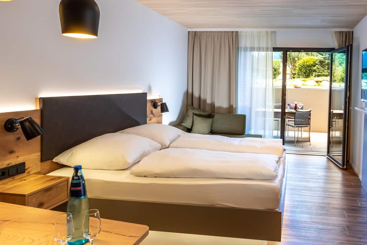 Ein Hotelzimmer mit zwei Betten, einem hölzernen Nachttisch, einer Wasserflasche und einem Tisch mit zwei Gläsern.