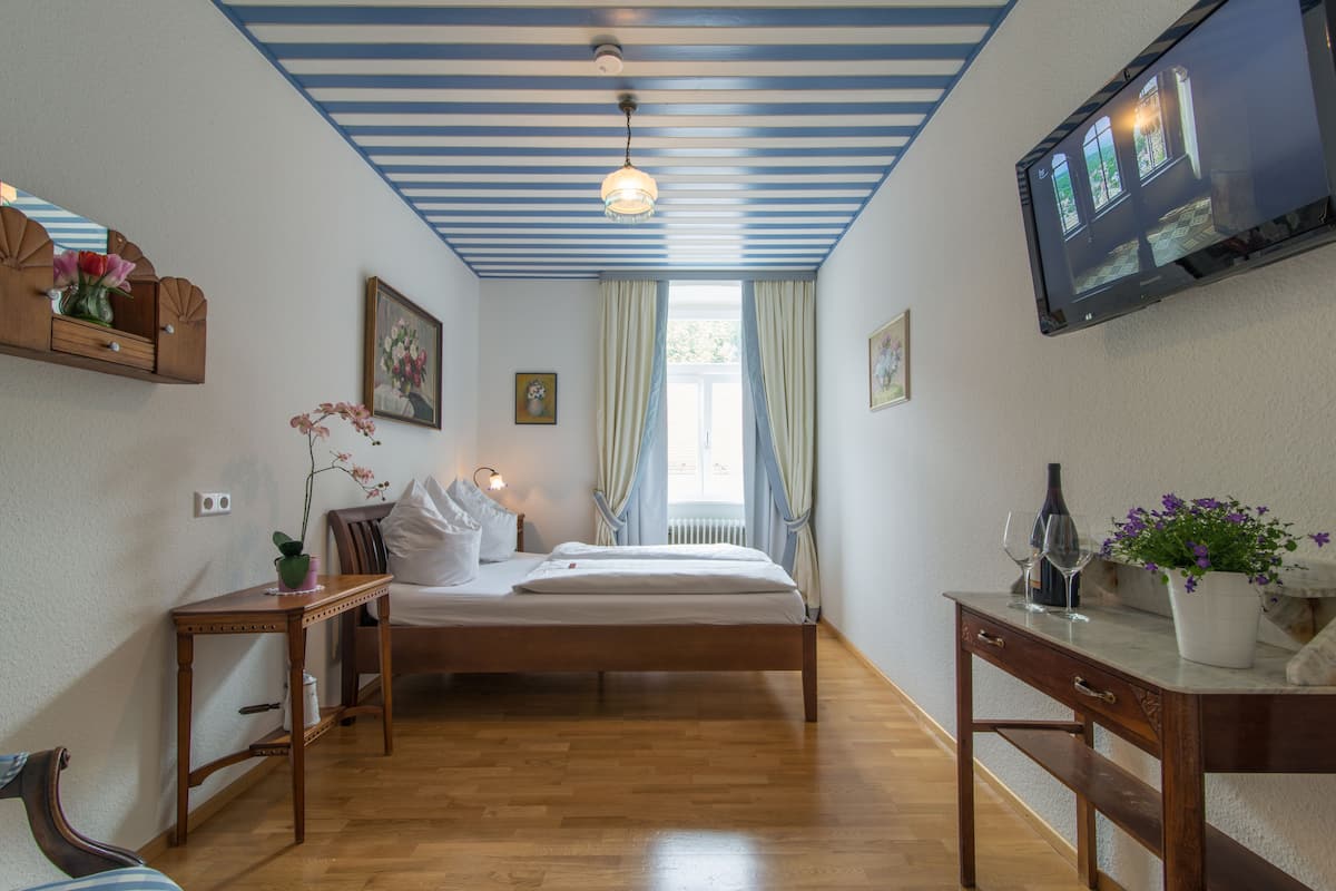 Ein Schlafzimmer mit einem hölzernen Bett, einem Nachttisch, einem an der Wand montierten Fernseher und einem Fenster mit Vorhängen.