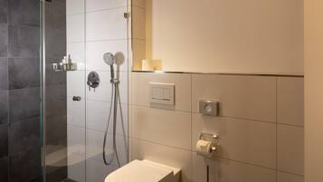 Une salle de bain moderne avec une douche à parois de verre, des toilettes et un porte-rouleau de papier toilette fixé au mur.