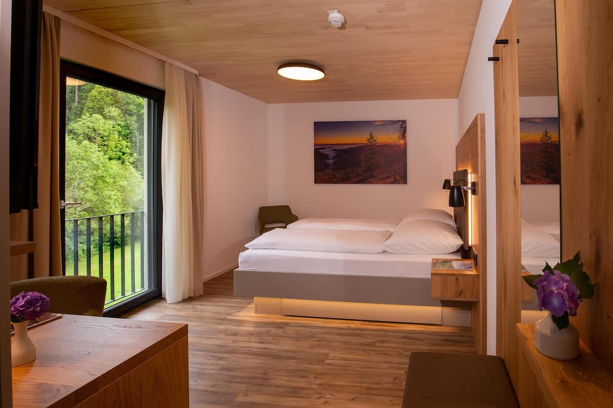 Ein modernes Schlafzimmer mit einem großen Bett, einem Nachttisch, einem Sessel und Balkonblick.