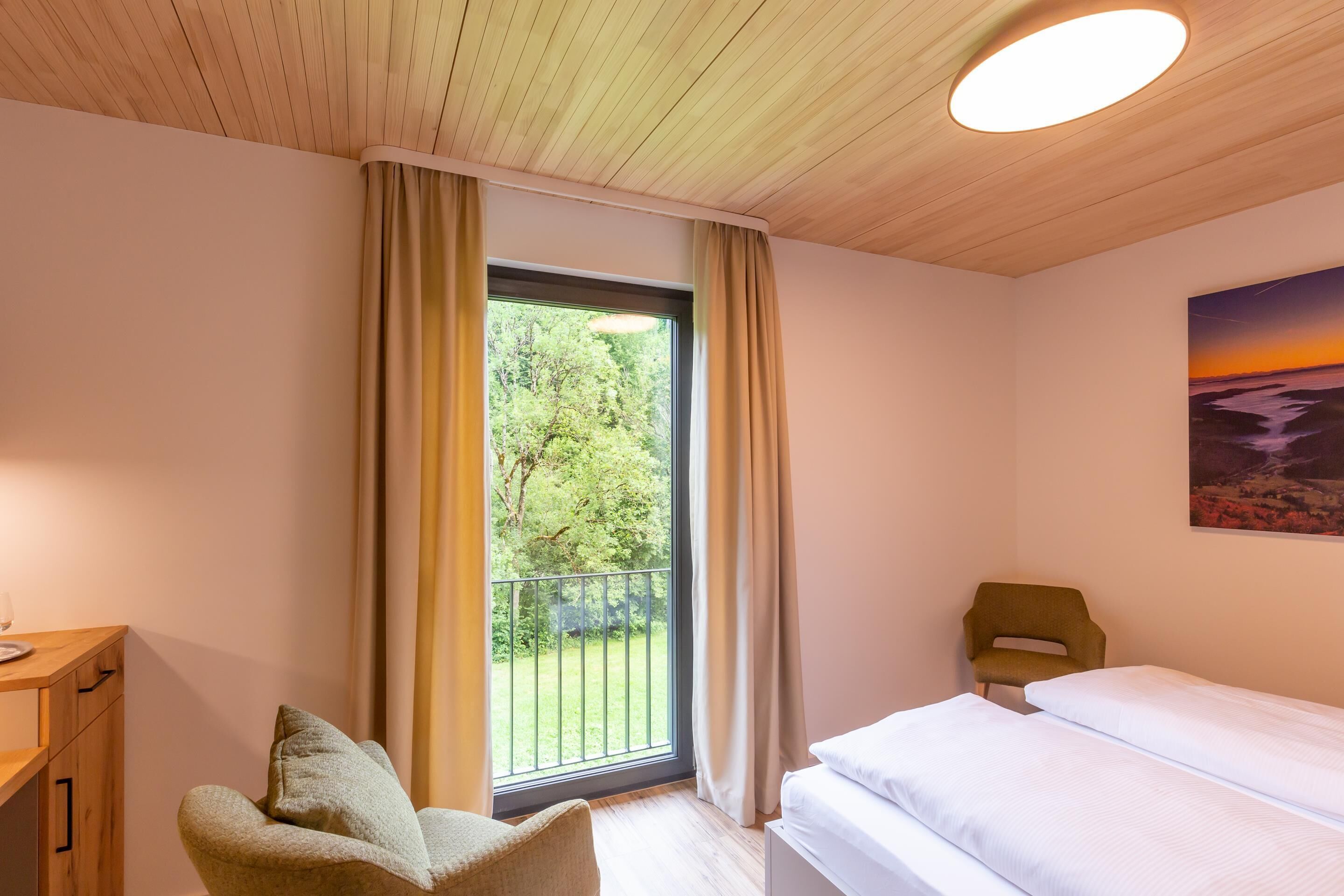 Un dormitorio con cama, una silla, un escritorio y una ventana con cortinas.