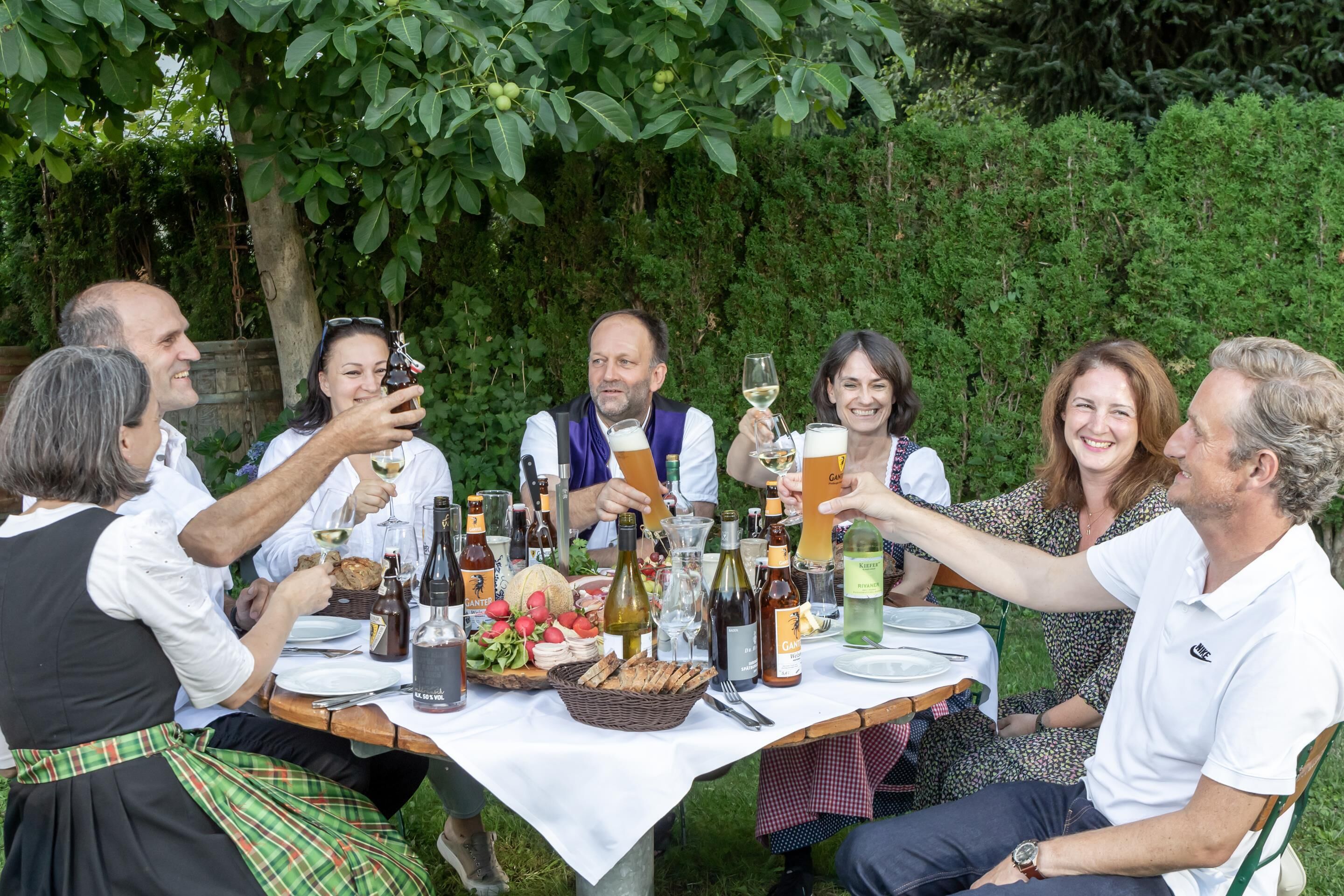 A group of people seated around a table with various food items and drinks, suggesting a social gathering or meal.