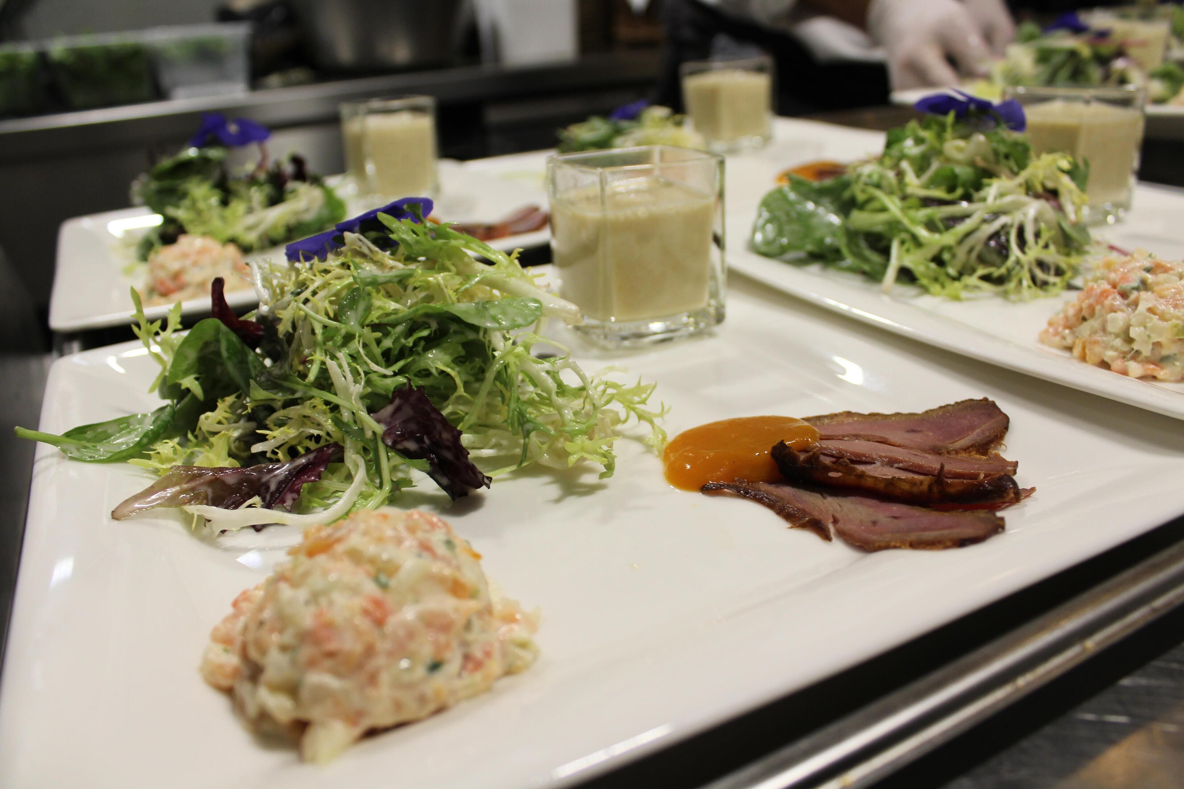 Una variedad de platos en un plato blanco, incluyendo una ensalada, una crema y trozos de carne.