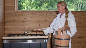 A person in a white robe using a wooden mallet to tap on a metal object, possibly a cooking pot, in a wooden cabin with a window overlooking greenery. - Goldener Adler Oberried - Hotel & Appartements (Oberried)