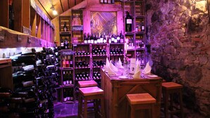 A wine cellar with wooden shelves and stools, featuring a variety of wine bottles and glasses. - Goldener Adler Oberried - Hotel & Appartements (Oberried)