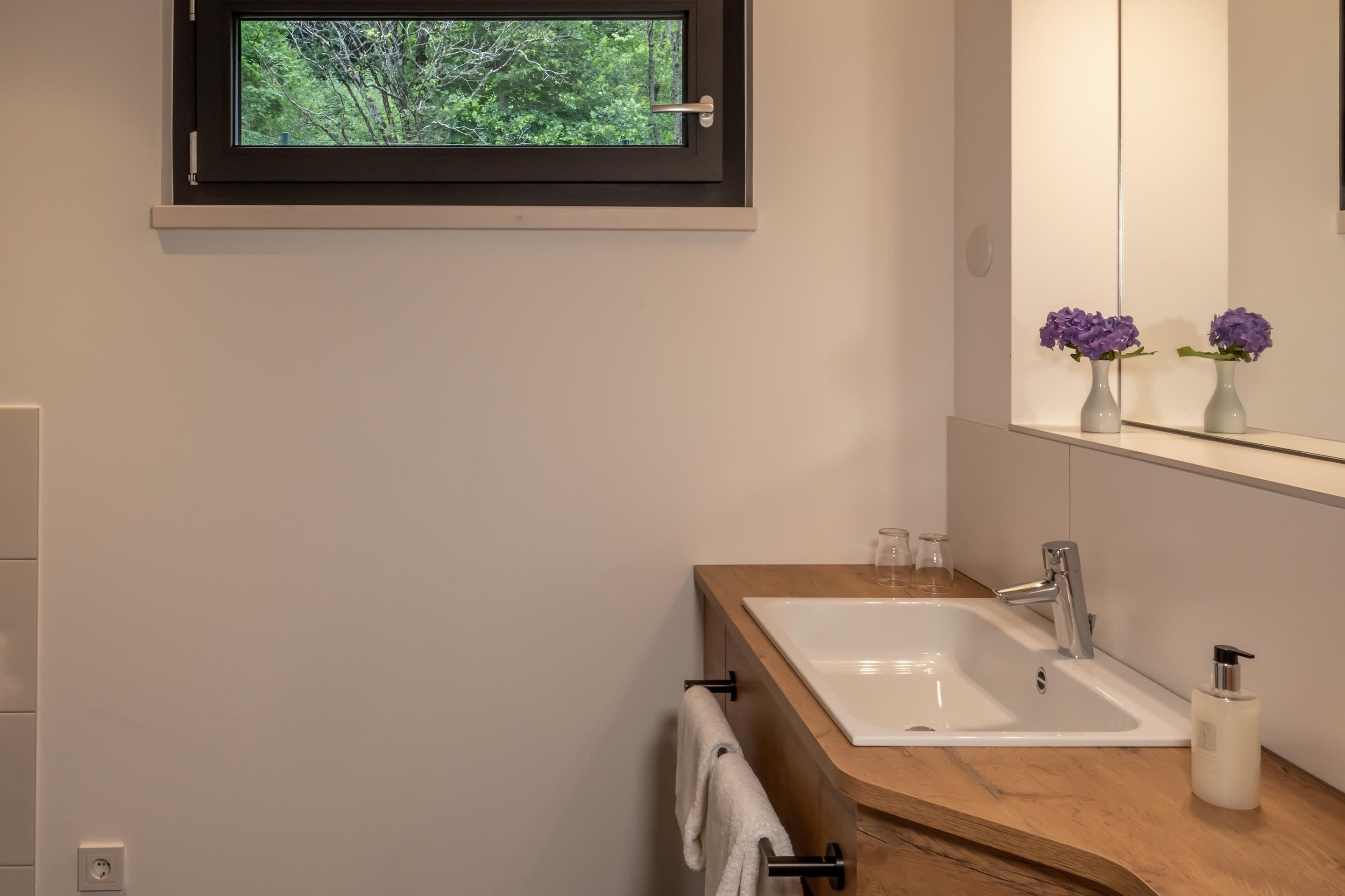 Een moderne badkamer met een houten wastafelmeubel, een witte wasbak en een spiegel erboven.