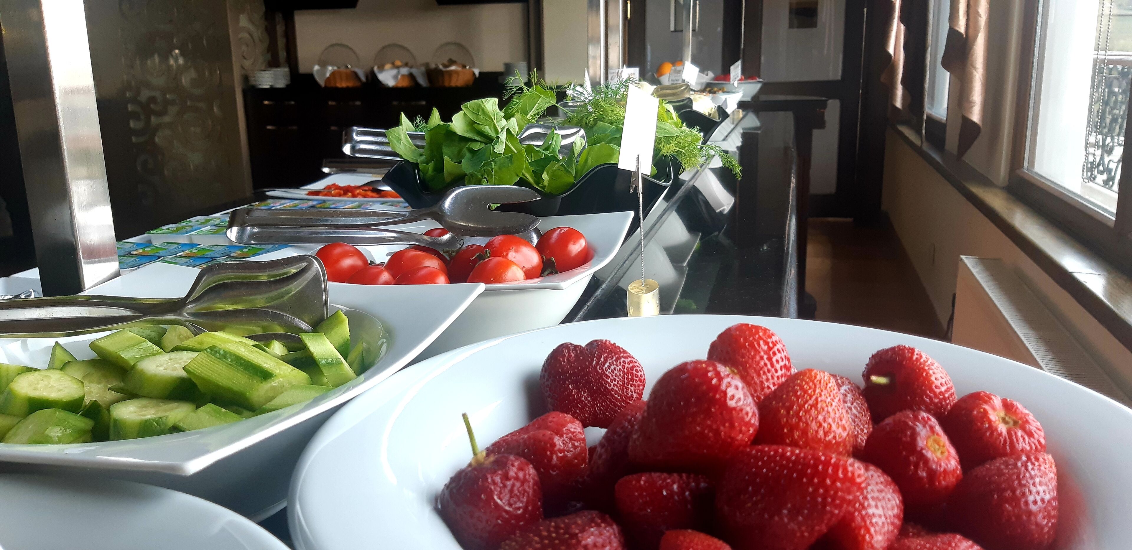 A buffet with various food items including sliced cucumbers, tomatoes, and strawberries.
