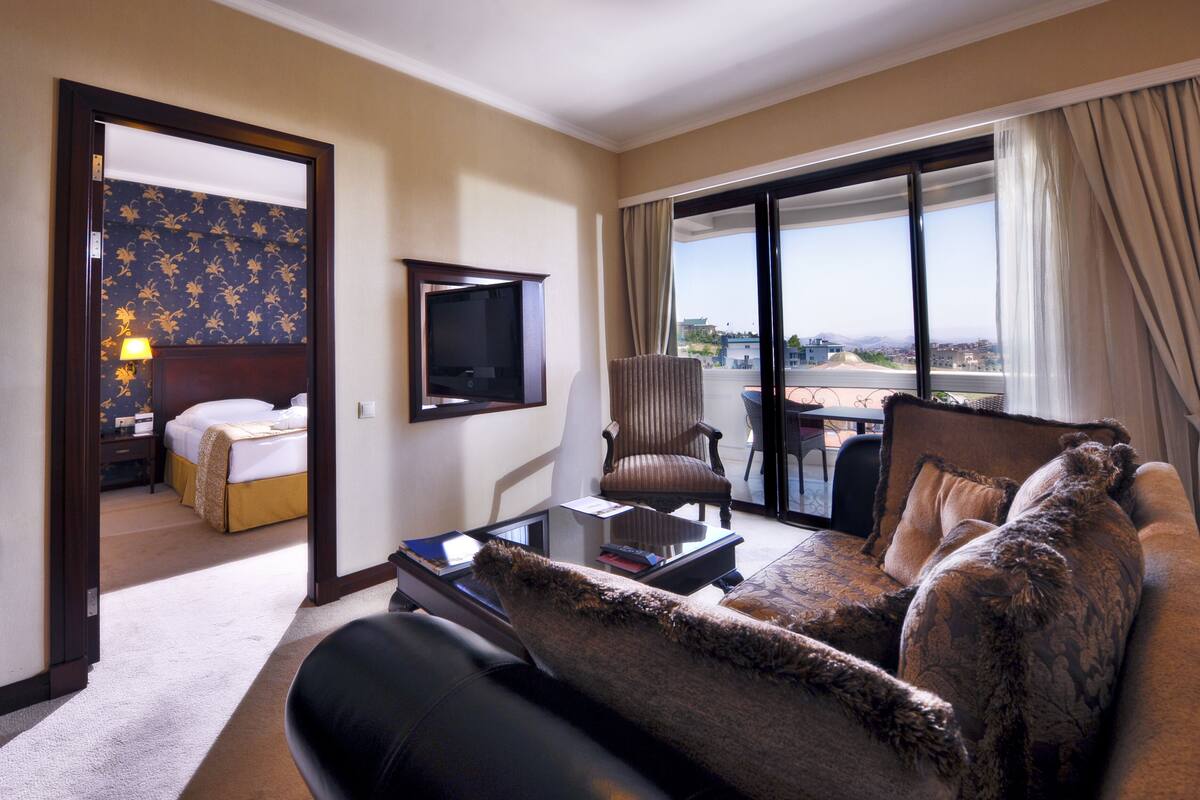 Ein Hotelzimmer mit einem großen Bett, einer Sitzecke, einem Fernseher und einem Balkon mit Blick.