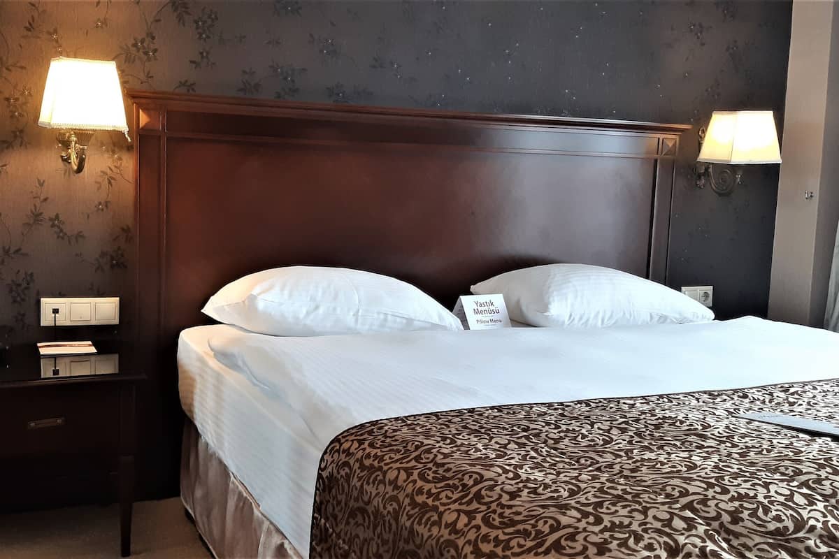 Ein Hotelzimmer mit einem großen Bett, zwei Nachttischlampen, einem Nachttisch mit Telefon und floralem Wandpapier.