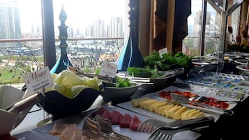 A buffet setup with various food items and a view of tall buildings in the background.