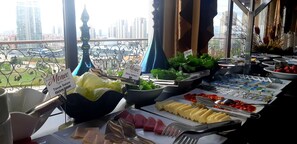 A buffet setup with various food items and a view of tall buildings in the background.