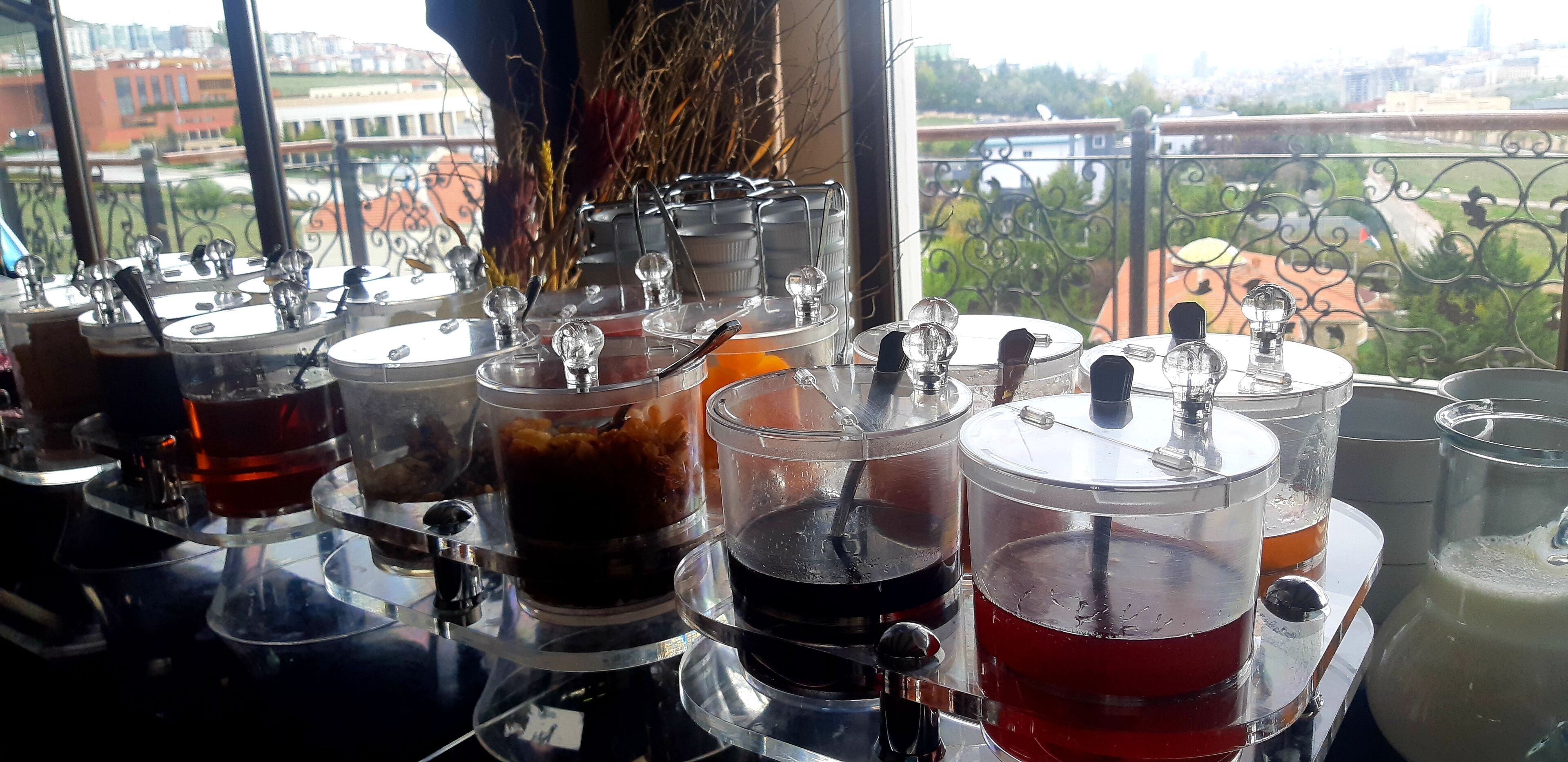 A bar with multiple cocktail shakers and glasses on a counter, with a view of a cityscape through a window.