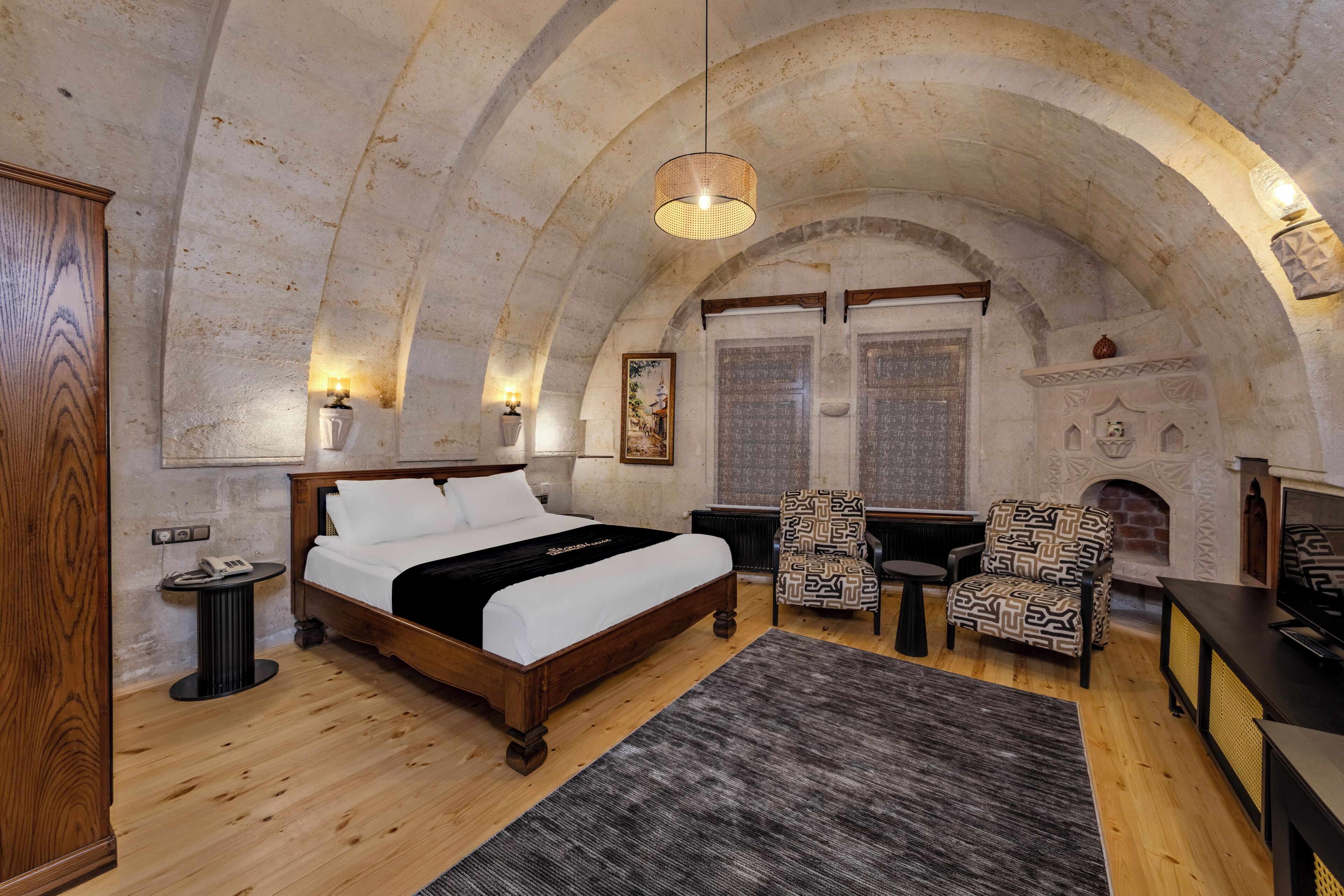 Un dormitorio con una cama de madera, chimenea, sillones estampados y techo de piedra.
