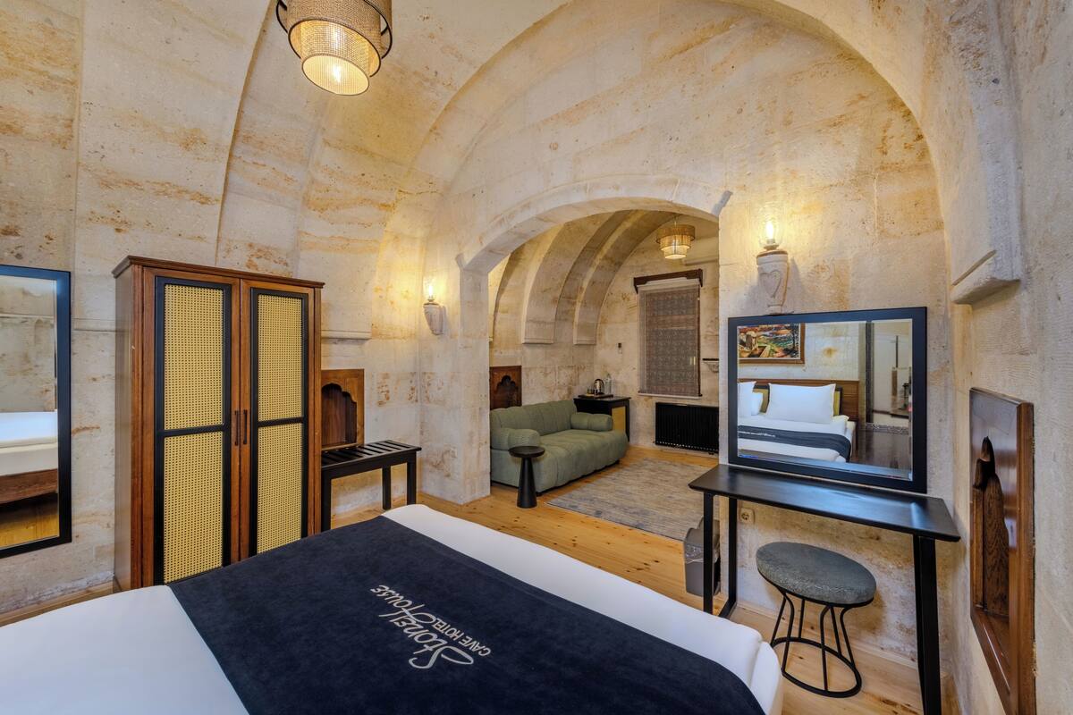 Ein Hotelzimmer mit einem Bett, einem Schreibtisch mit Stuhl, einem Sofa, einem Spiegel und einer gewölbten Decke.