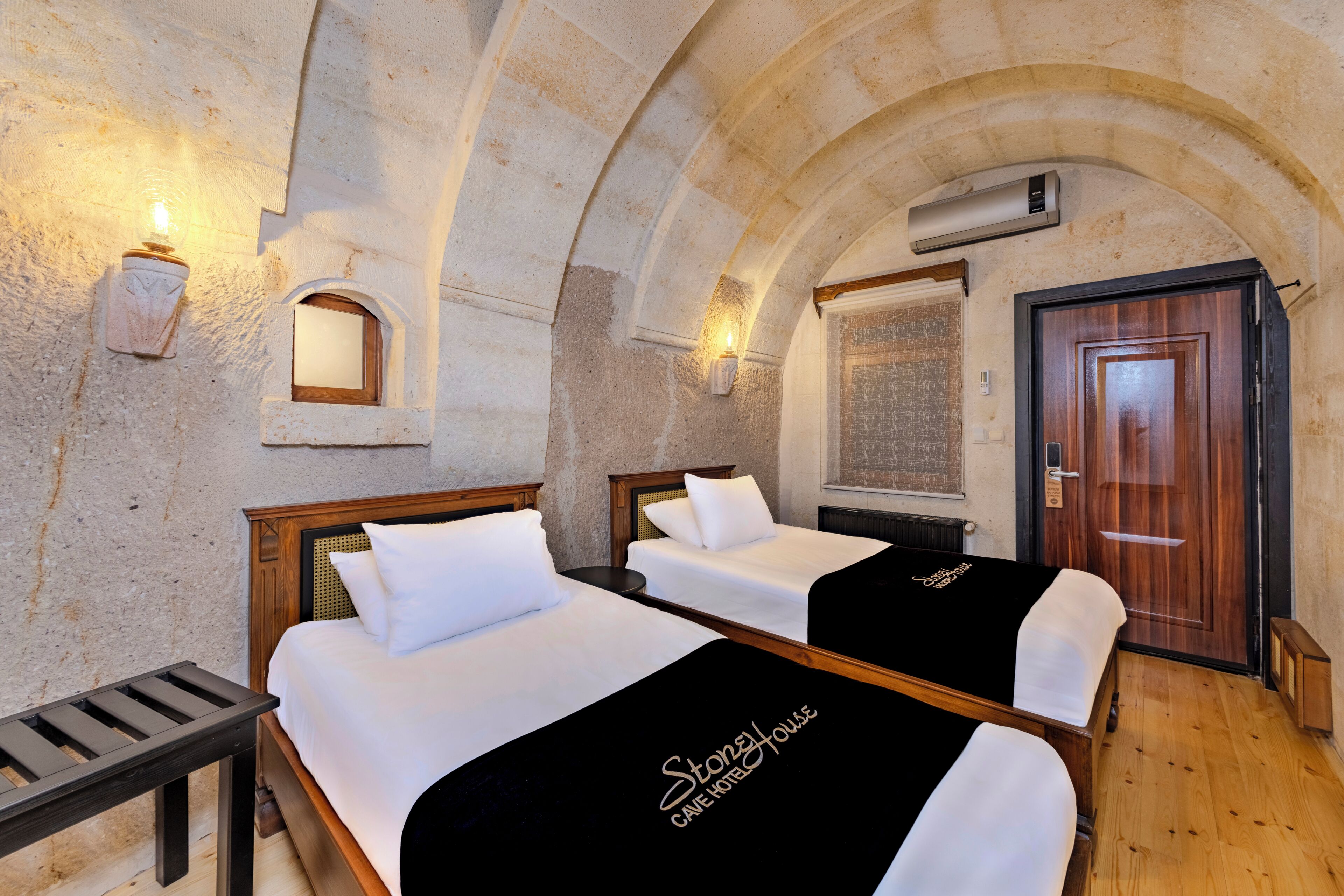 A hotel room with two beds, a wooden bench, stone walls, and a wooden door.