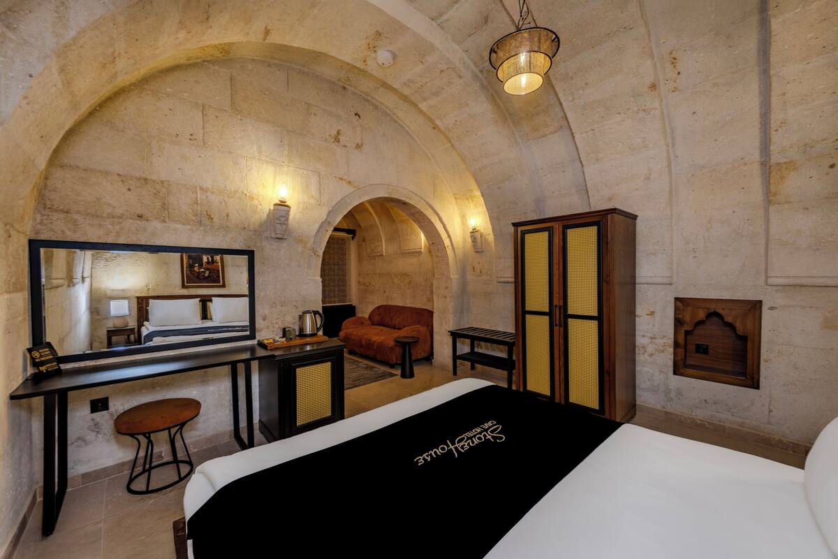 Ein Hotelzimmer mit einer Decke aus Steinbogen, einem Bett, einem Schreibtisch mit Stuhl, einem kleinen Tisch und einem Spiegel.