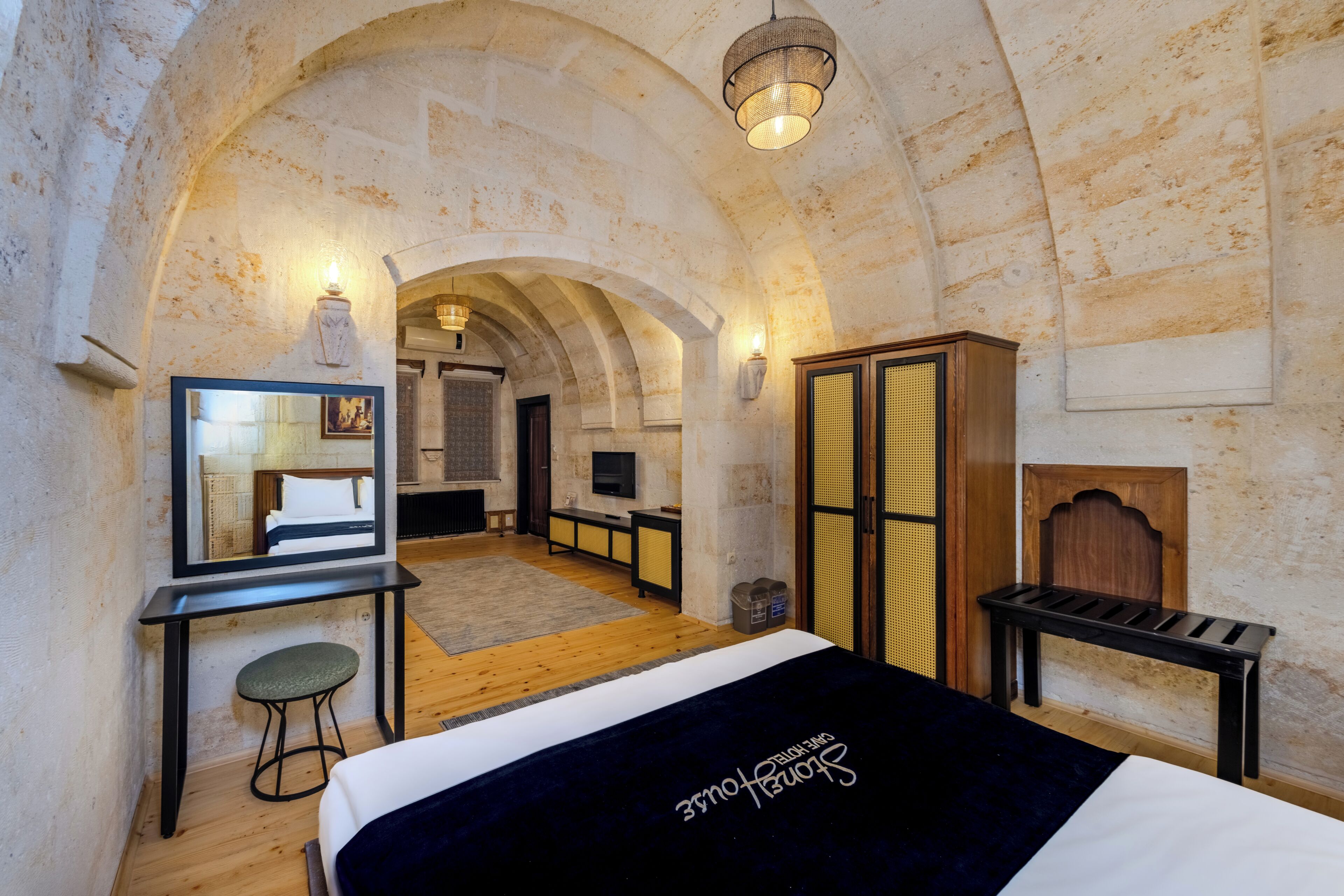 A room with a bed, a desk, a chair, a television, and an arched ceiling.