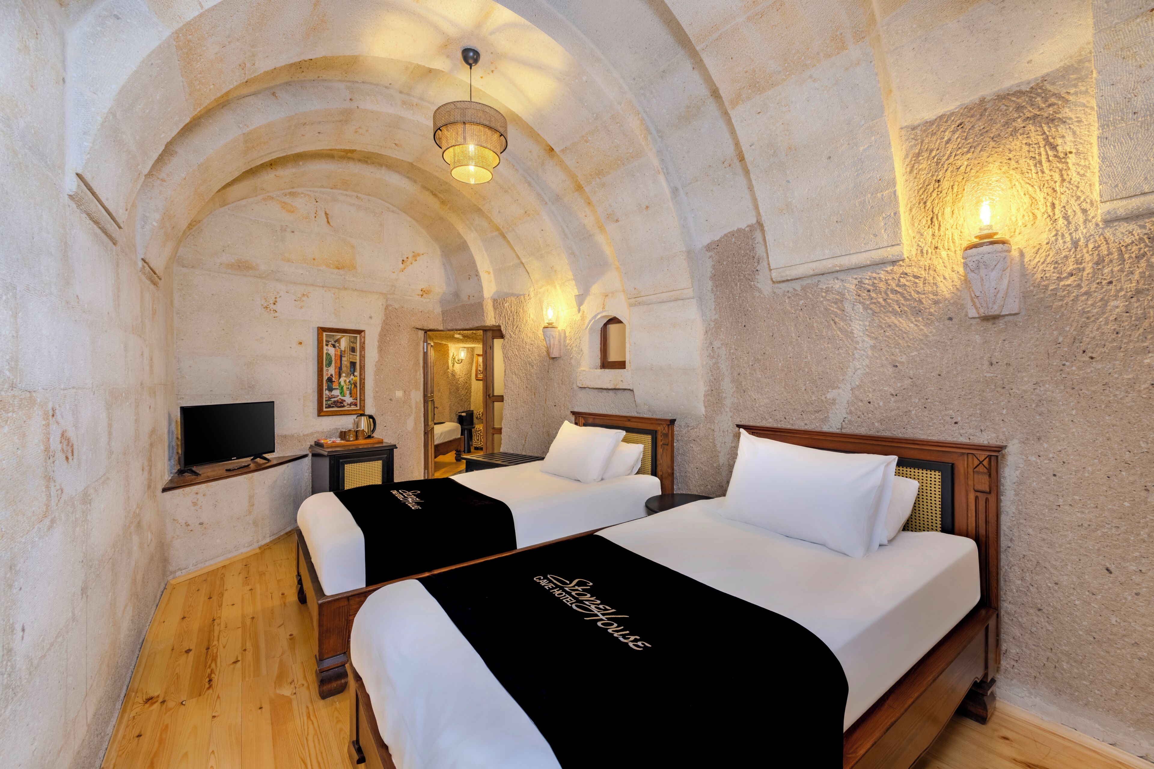 Habitación con dos camas, televisión y pared de piedra.