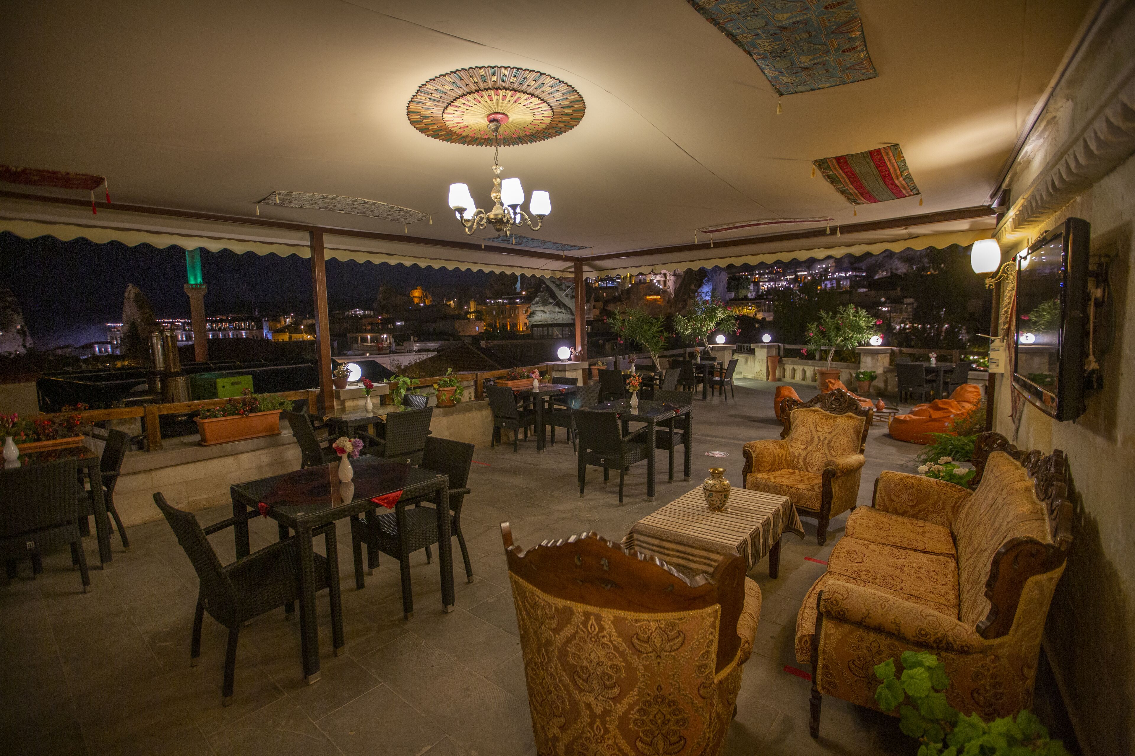 An outdoor seating area with tables and chairs, a decorative ceiling light, and a view of the cityscape at night.