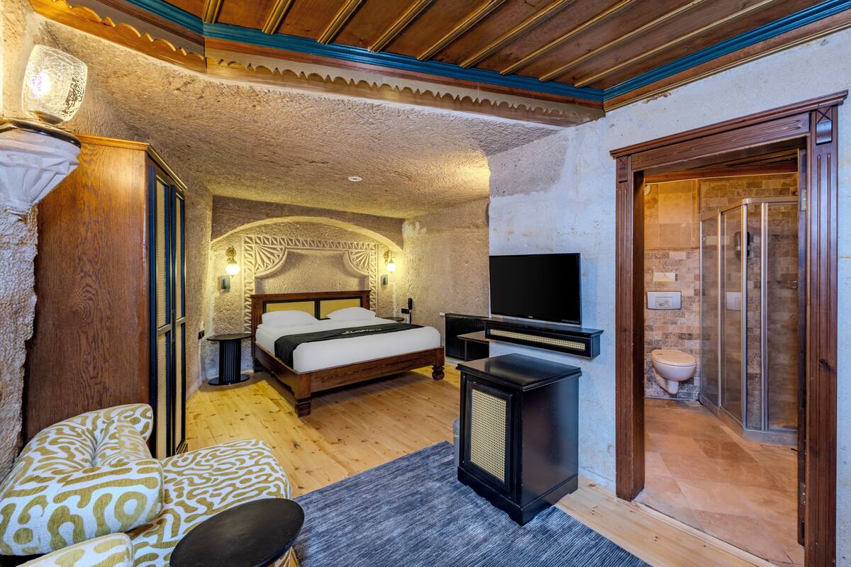 Ein Schlafzimmer mit Bett, Nachttischen, einem Fernseher und einem Badezimmer mit Dusche und Toilette.