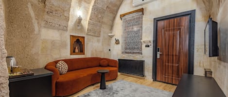 Una habitación con pared de piedra, puerta de madera, un sofá, una mesita y un radiador.