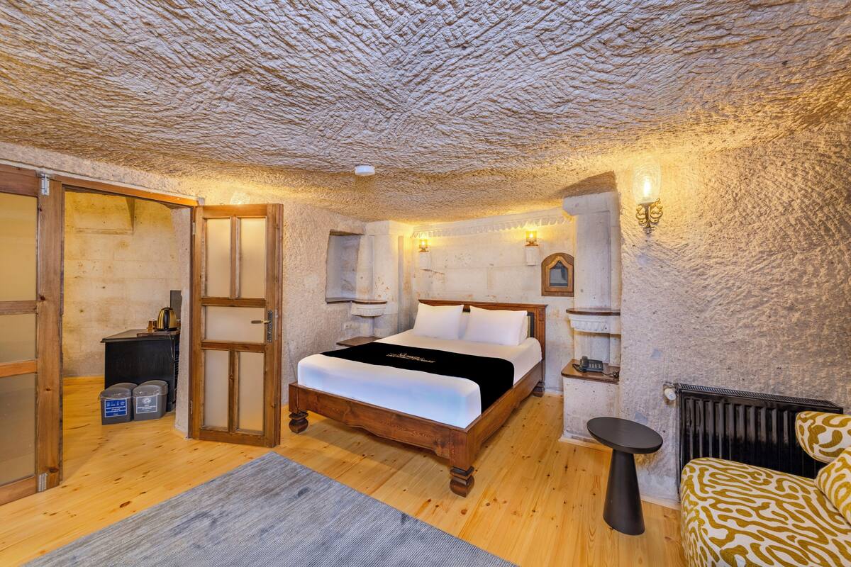 Ein Schlafzimmer mit einem hölzernen Bett, einem kleinen Tisch, einem Stuhl, einem Heizkörper und einer Steindecke.