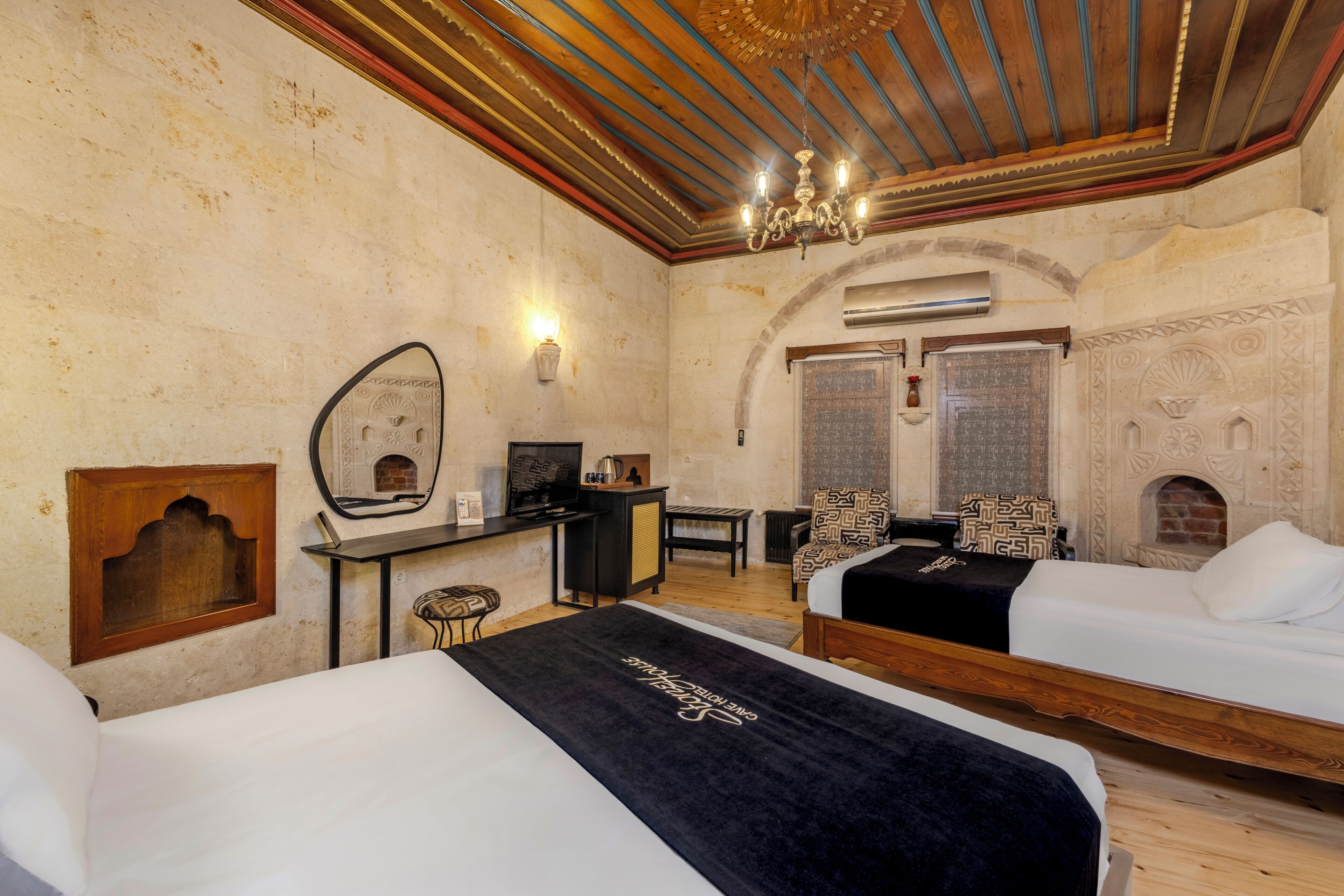 A room with two beds, a desk with a computer, a mirror, and a fireplace.